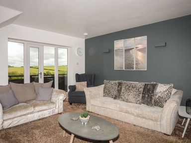 A living room with two sofas a dark armchair an oval coffee table and a triptych beach wall art at The Old Coal Yard in Cemaes Bay