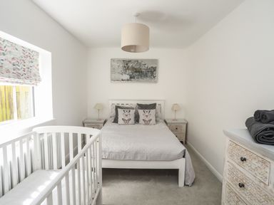 A bedroom with a double bed and a baby crib next to a window with patterned blinds at The Old Coal Yard in Cemaes Bay