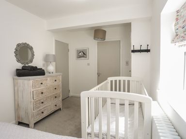 A nursery room with a white crib a wooden dresser with black towels a lamp a round mirror and two closed doors at The Old Coal Yard in Cemaes Bay