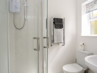 A bathroom with a shower cubicle a heated towel rail with towels a toilet with toilet paper and a window at The Old Coal Yard in Cemaes Bay