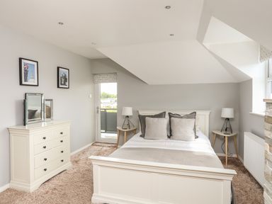 A bedroom with a white bed and dresser with two bedside tables and lamps at The Old Coal Yard in Cemaes Bay