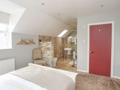 A bedroom with a bed a chair and an en suite bathroom with a glass shower and a red door at The Old Coal Yard in Cemaes Bay