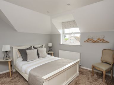A bedroom with a white bed frame two side tables with lamps a window with a blind and a chair at The Old Coal Yard in Cemaes Bay