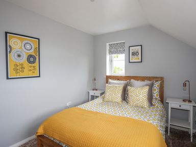 A bedroom with a double bed yellow and grey bedding and pillows two white bedside tables with lamps and wall art at The Old Coal Yard in Cemaes Bay
