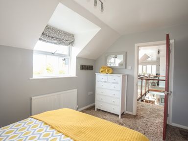 A bedroom with a patterned bedspread and yellow blanket next to a window and white chest of drawers with yellow towels at The Old Coal Yard in Cemaes Bay