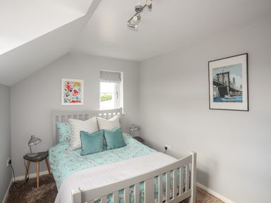 A bedroom with a bed with teal bedding two bedside tables with lamps and wall art at The Old Coal Yard in Cemaes Bay