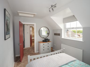 A bedroom with a bed chest of drawers and a round mirror by the window at The Old Coal Yard in Cemaes Bay