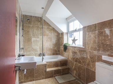 A bathroom with a bathtub shower sink toilet tiled walls and a window with a star decoration at The Old Coal Yard in Cemaes Bay