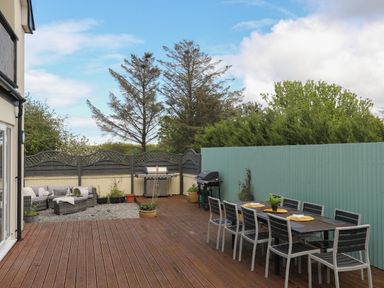 An outdoor patio with a dining table and chairs a sofa set two grills and potted plants at The Old Coal Yard in Cemaes Bay