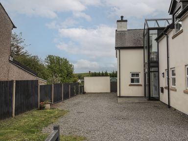 A gravel driveway beside a cream house with black fencing and green trees at The Old Coal Yard in Cemaes Bay
