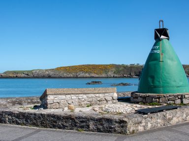 A coastal scene with a stone wall and green buoy near the water at The Old Coal Yard in Cemaes Bay