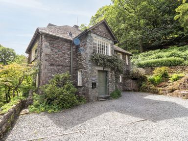 A stone house with gravel driveway surrounded by plants and trees at Huntingstile Lodge in Grasmere