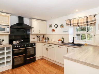 A kitchen with white cabinets a black oven stove and hood a microwave and a window with patterned curtains at Huntingstile Lodge in Grasmere