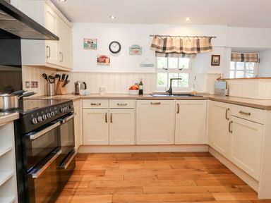 A kitchen with white cabinets a black stove a wooden floor and checkered curtains at Huntingstile Lodge in Grasmere