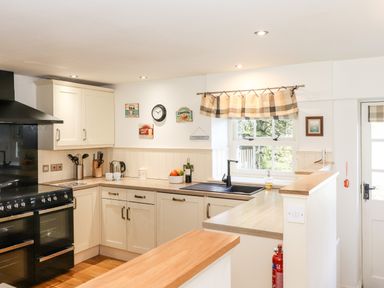 A kitchen with white cabinets a black stove a window above the sink and a wooden countertop at Huntingstile Lodge in Grasmere
