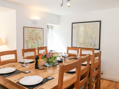 A dining room with a wooden table set for eight with plates glasses wine bottle and flower centerpiece at Huntingstile Lodge Grasmere