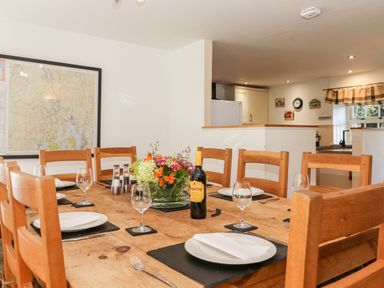 A dining room with a wooden table set with plates wine glasses and a flower centerpiece at Huntingstile Lodge in Grasmere