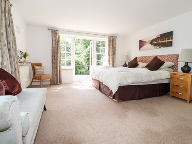 A bedroom with a bed sofa chair nightstand lamps and large windows at Huntingstile Lodge in Grasmere