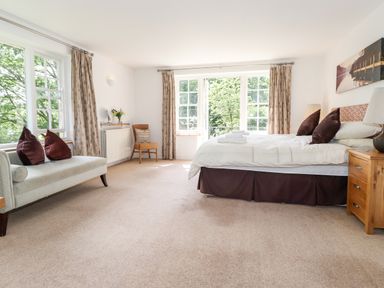 A bedroom with a bed side table a chair and a bench with pillows at Huntingstile Lodge in Grasmere