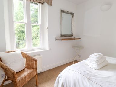 A bedroom with a wicker chair near a window folded towels on a bed a mirror and a small round table at Huntingstile Lodge in Grasmere
