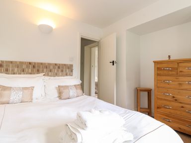 A bedroom with a bed a wooden dresser a small stool and an open door at Huntingstile Lodge in Grasmere