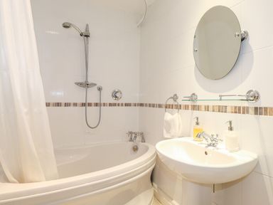 A bathroom with a bathtub shower and sink with soap dispensers at Huntingstile Lodge in Grasmere