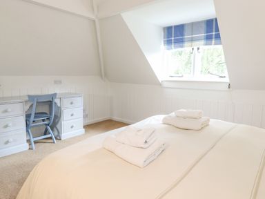 A bedroom with a bed topped with folded towels a desk with drawers and a blue chair under a window with a blue checkered blind at Huntingstile Lodge in Grasmere