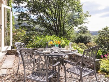 An outdoor patio with a metal table and chairs set with cups plates and flowers at Huntingstile Lodge in Grasmere