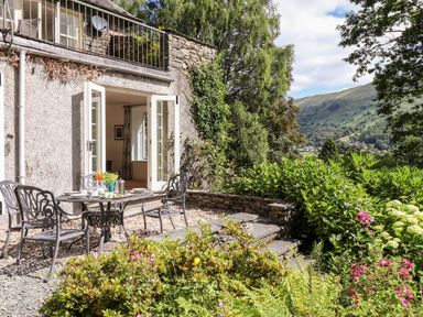 A garden patio with metal table and chairs outside a house with open double doors at Huntingstile Lodge in Grasmere