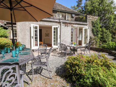 An outdoor patio with metal tables and chairs set with blue glassware outside a stone building at Huntingstile Lodge in Grasmere