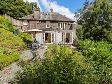 A garden with patio furniture and an umbrella outside a stone house at Huntingstile Lodge in Grasmere