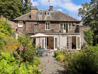 A garden with patio tables and umbrella outside a stone house with upper and lower balconies at Huntingstile Lodge in Grasmere