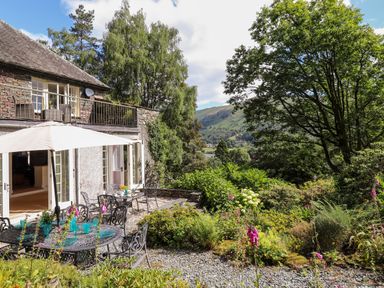 An outdoor patio with tables and chairs under an umbrella next to a stone house and garden at Huntingstile Lodge in Grasmere