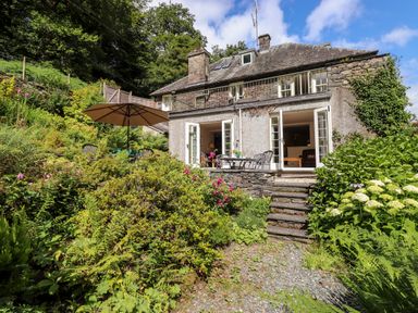 A garden with flowers and furniture outside a stone house with open doors at Huntingstile Lodge in Grasmere