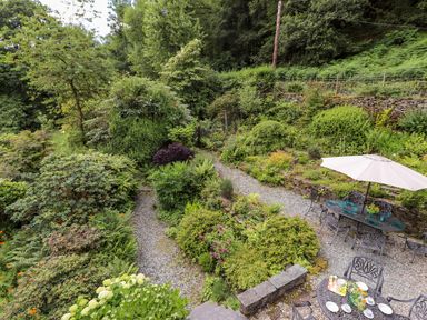 A garden with gravel pathways surrounded by greenery and outdoor metal tables and chairs at Huntingstile Lodge in Grasmere