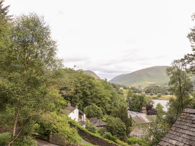 A hillside view with houses trees a lake and mountains in the background at Huntingstile Lodge in Grasmere