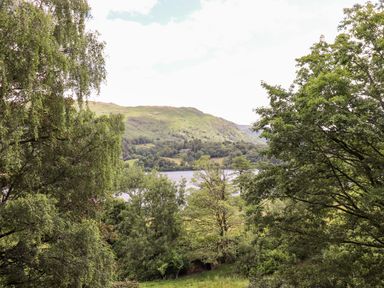 A landscape with trees in the foreground a lake and hills in the background at Huntingstile Lodge in Grasmere