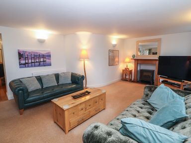 A living room with two sofas a wooden coffee table a television and lamps at Huntingstile Lodge in Grasmere