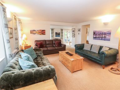 A living room with three sofas a wooden coffee table and landscape paintings at Huntingstile Lodge in Grasmere