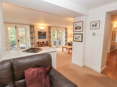 A living room with a brown leather sofa a wooden coffee table paintings on the wall and glass doors leading outside at Huntingstile Lodge in Grasmere
