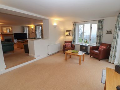 A living room with two brown leather armchairs a wooden table and a window at Huntingstile Lodge in Grasmere