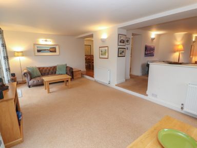 A living room with a brown sofa green cushions wooden tables and framed pictures on walls at Huntingstile Lodge in Grasmere