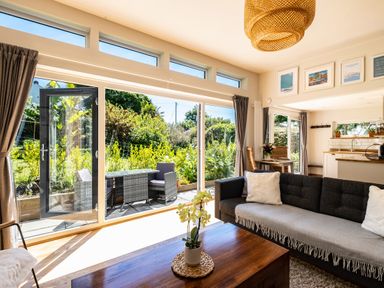 A living room with a sofa table and large windows looking out to a garden at Chi Lowarth in Porthleven