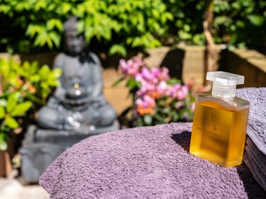 A bottle of aromatherapy oil on towels with a Buddha statue and plants in the background at Chi Lowarth in Porthleven