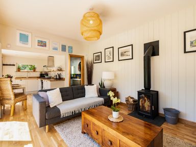 A living room with a gray sofa and wood stove next to a wooden coffee table at Chi Lowarth in Porthleven