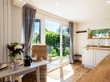 A kitchen with a table set for breakfast and glass doors opening to a garden at Chi Lowarth in Porthleven