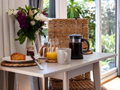 A table with a cup, a glass of orange juice, a French press, toast, and a croissant with flowers in a vase at Chi Lowarth in Porthleven