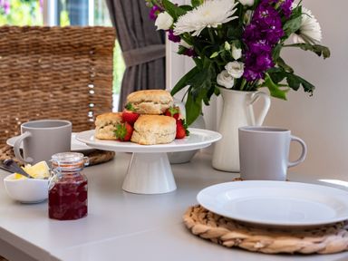 A table set with scones and strawberries a jar of jam mugs and a vase of flowers at Chi Lowarth in Porthleven