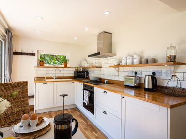 A kitchen with wooden countertops white cabinets open shelves and a breakfast table at Chi Lowarth in Porthleven