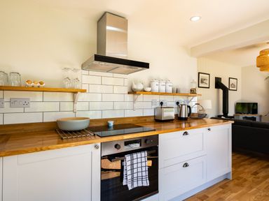 A kitchen with wooden countertops white cabinets a stovetop oven toaster kettle and shelves with jars at Chi Lowarth in Porthleven